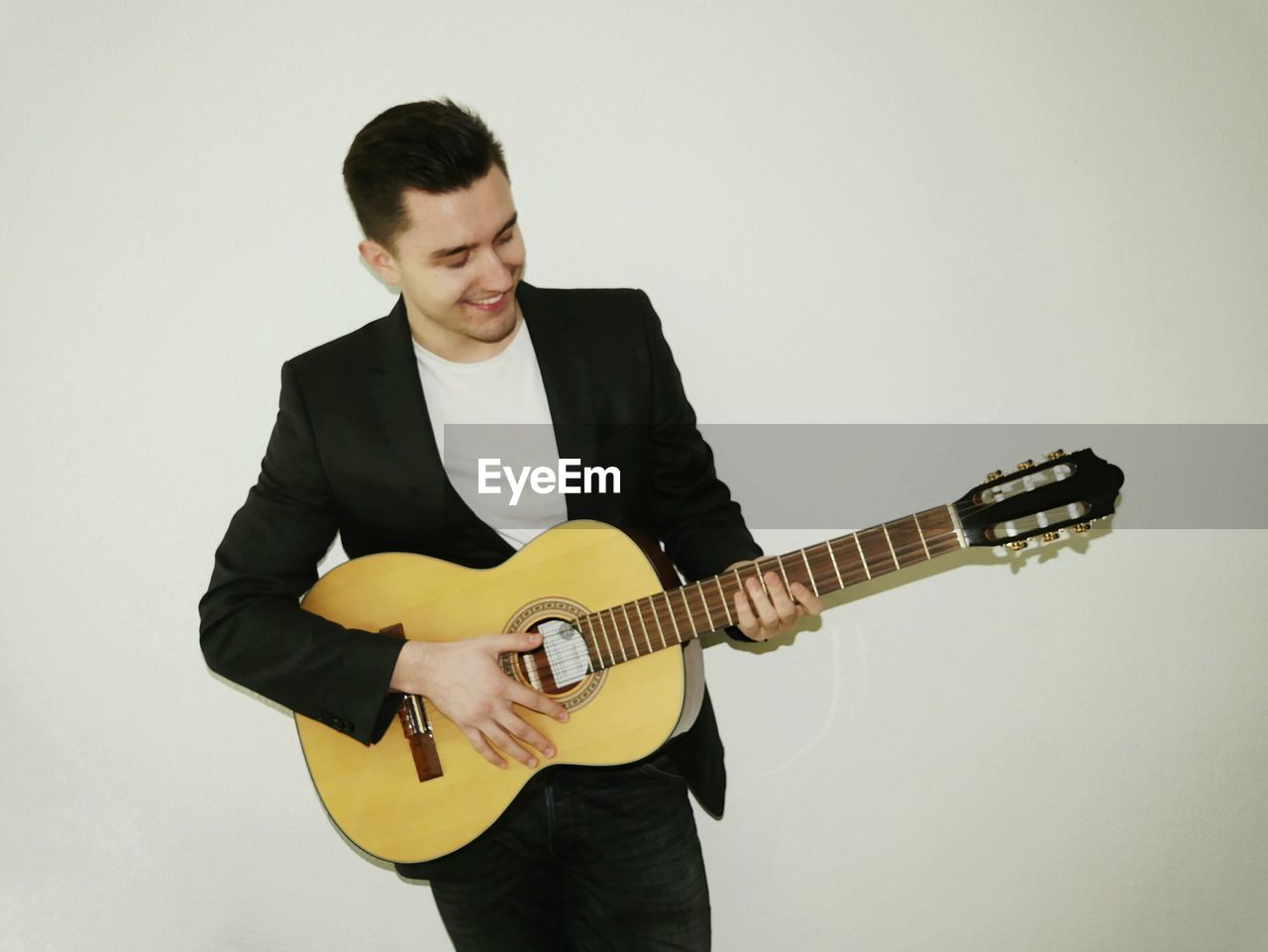 Smiling man playing guitar while standing against white background