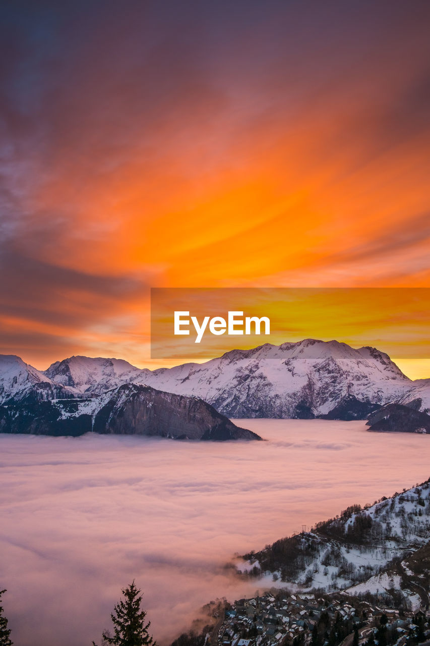 Scenic view of lake by snowcapped mountains against orange sky