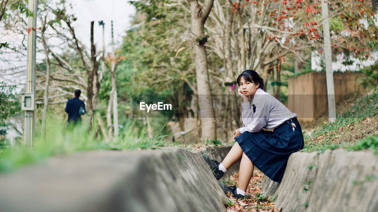 Portrait of young woman sitting against plants in park