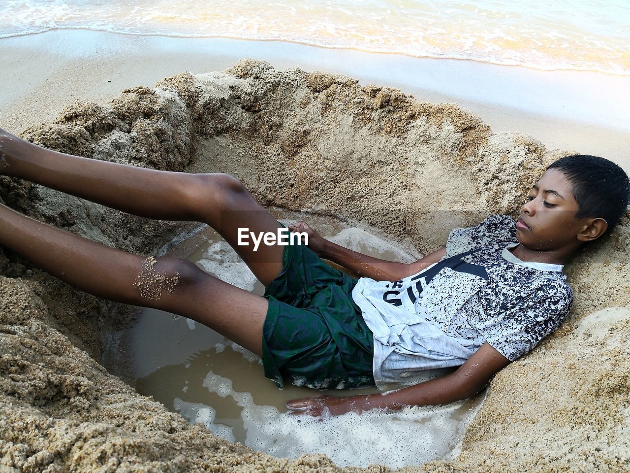 High angle view of boy lying in pit at beach