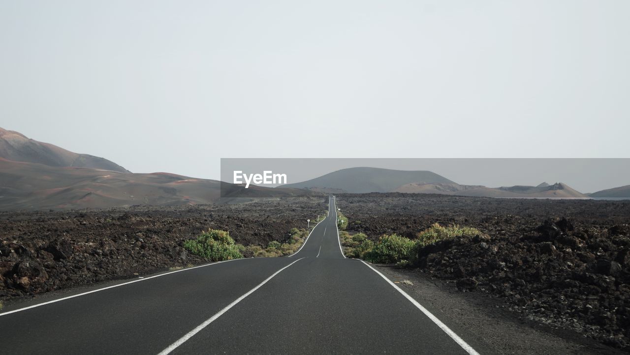 Empty road by mountains against clear sky