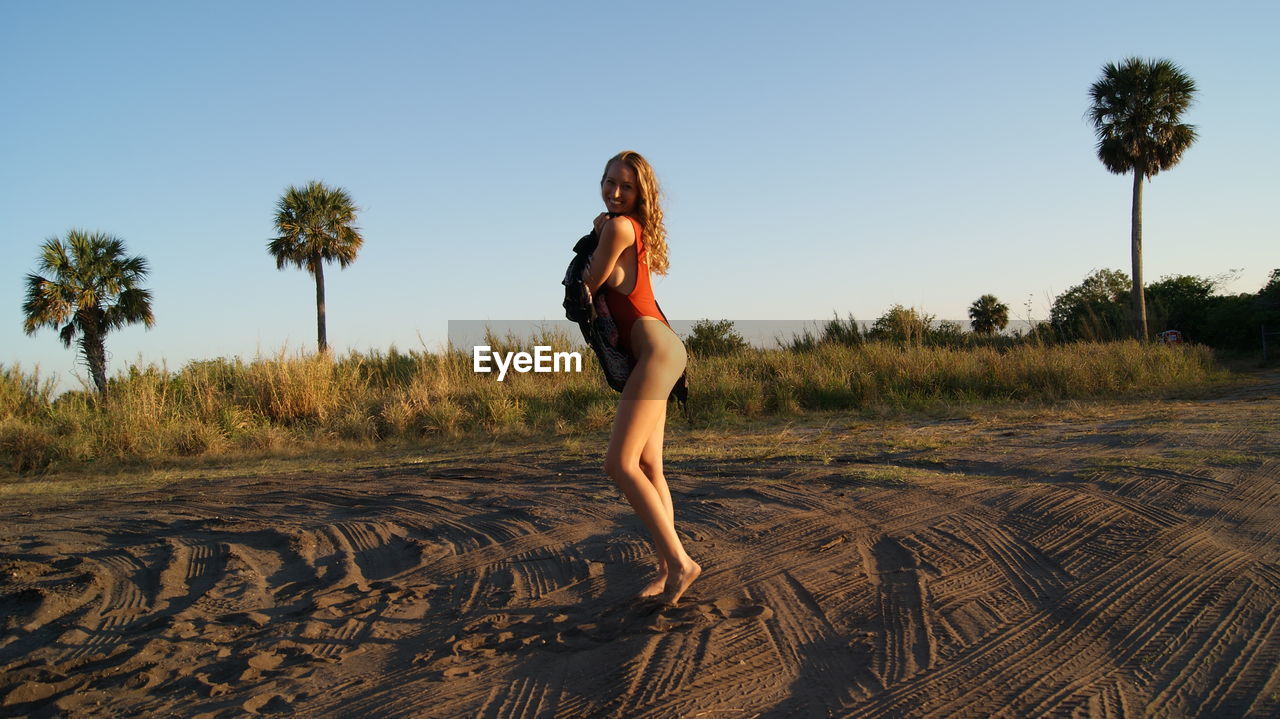 Side view full length of young woman wearing one piece swimsuit standing on sand