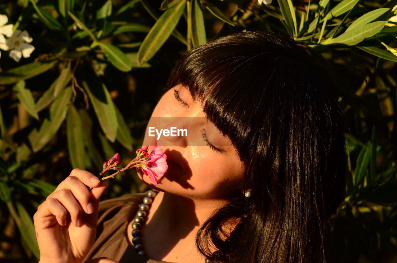one person, women, food, adult, food and drink, female, portrait, headshot, plant, young adult, eating, holding, nature, person, flower, hairstyle, fruit, freshness, leaf, lifestyles, healthy eating, brown hair, plant part, leisure activity, happiness, long hair, outdoors, smiling, wellbeing, black hair, biting, emotion, singing, hand, beauty in nature, spring