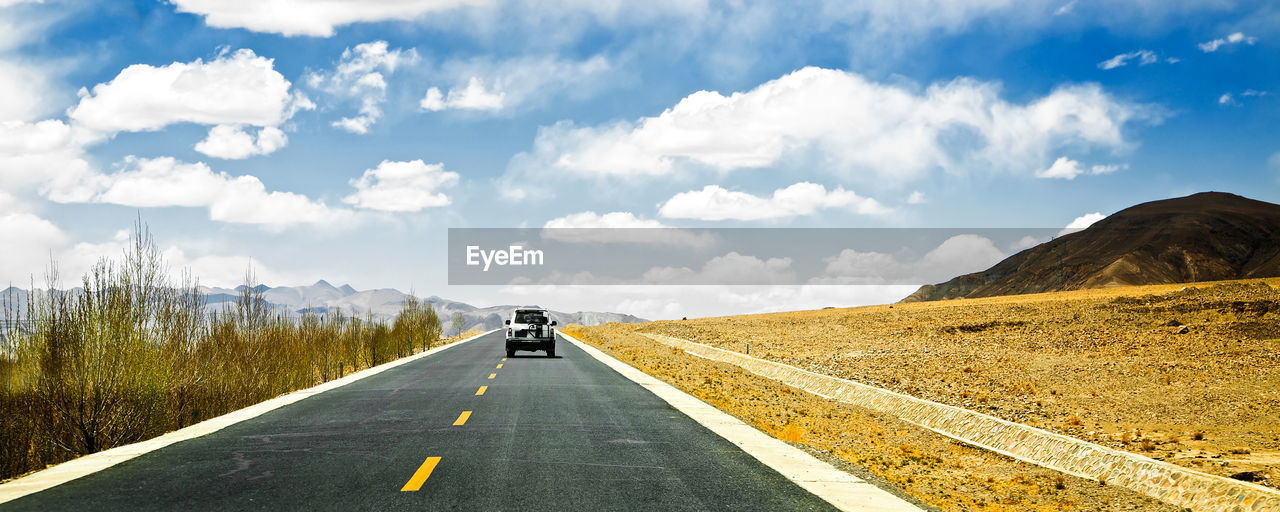 Vehicles on road against cloudy sky