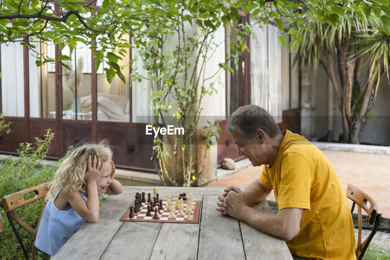 Granddaughter and grandfather enjoying chess in garden