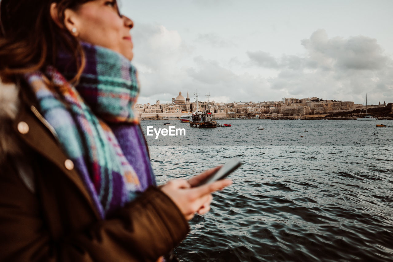 Young woman using mobile phone by sea against sky