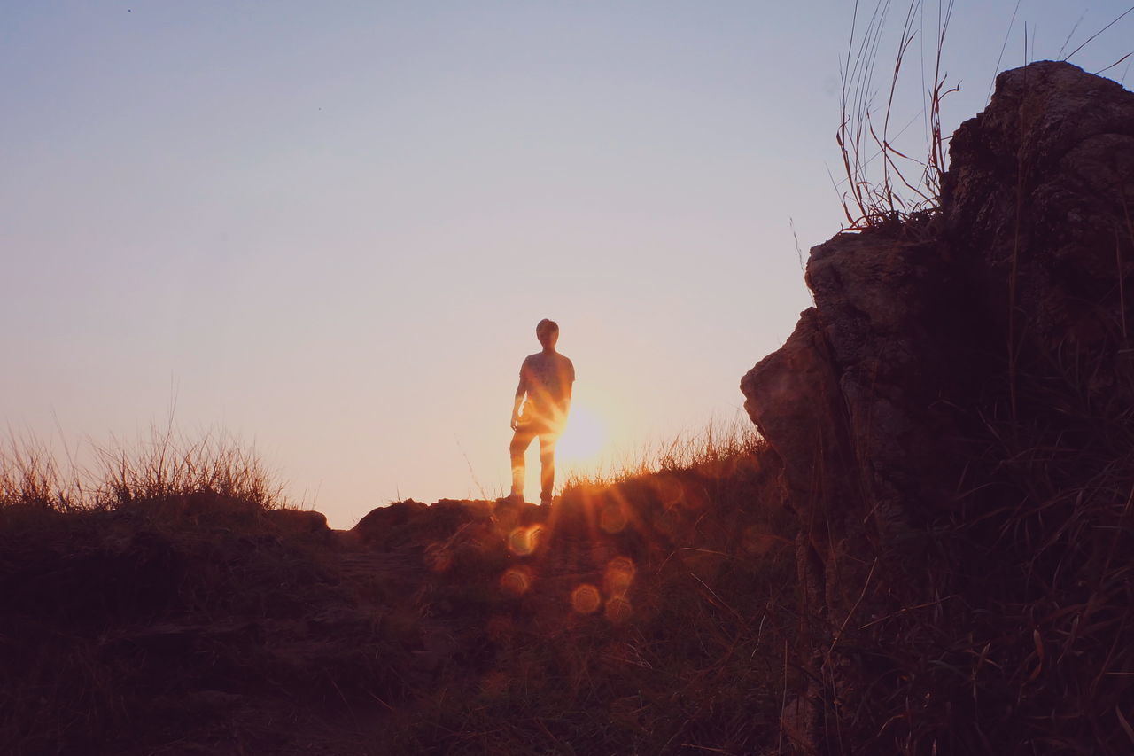 Low angle view of man standing on hill against clear sky during sunset