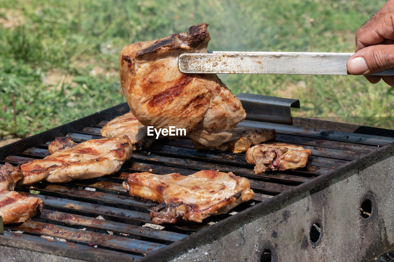 Cropped hand of meat on barbecue grill