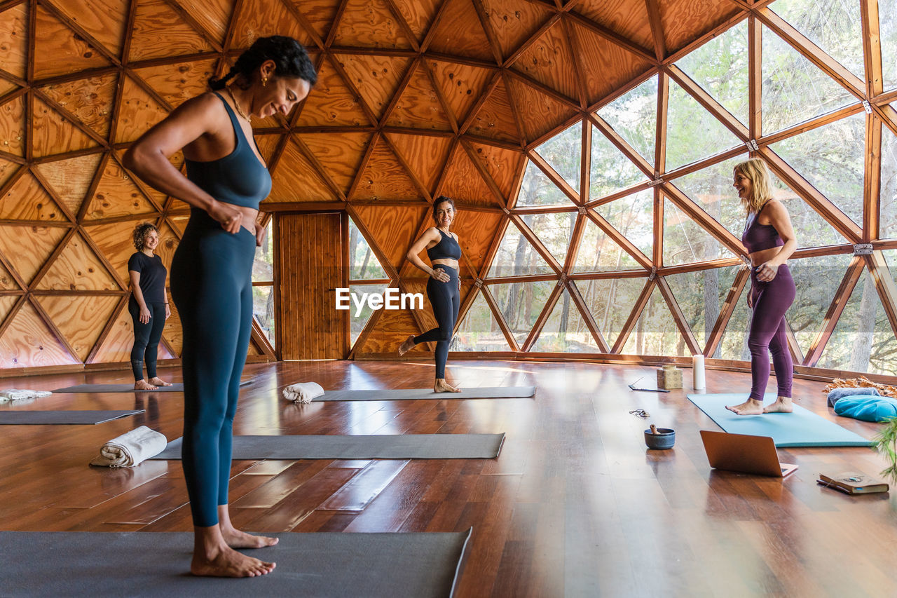 Full body side view of happy women preparing to practice yoga in light studio