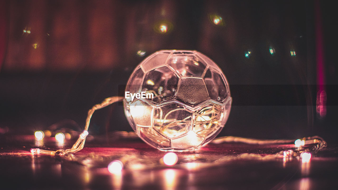 CLOSE-UP OF ILLUMINATED GLASS BALL WITH REFLECTION ON TABLE