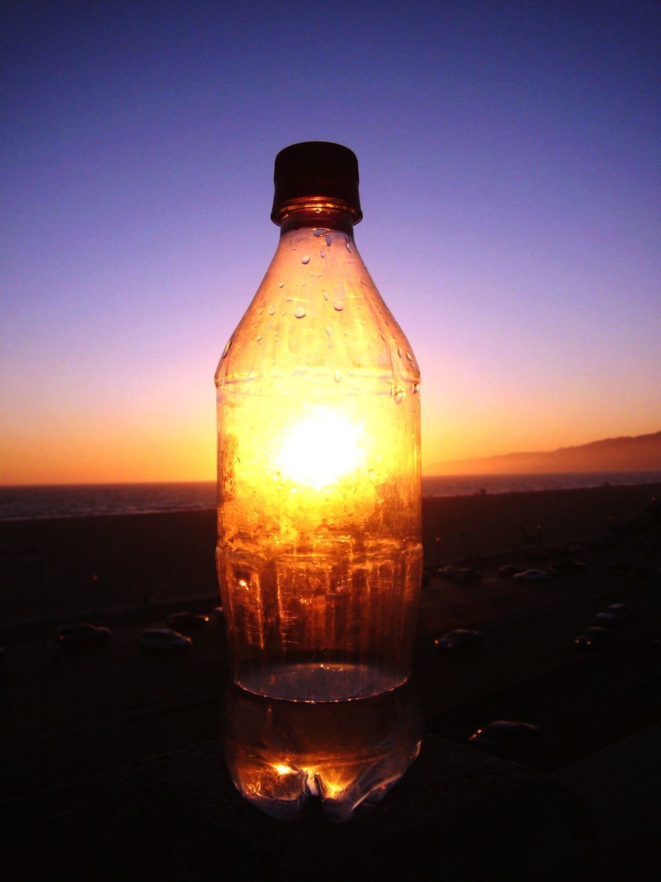 Sun seen through plastic bottle on table over beach against clear sky