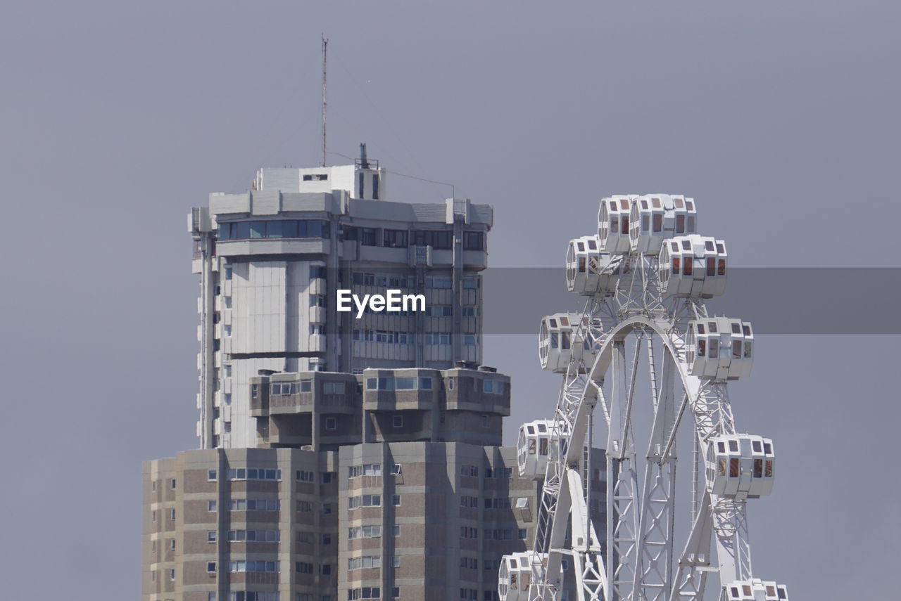 Wheel and buildings in city against clear sky
