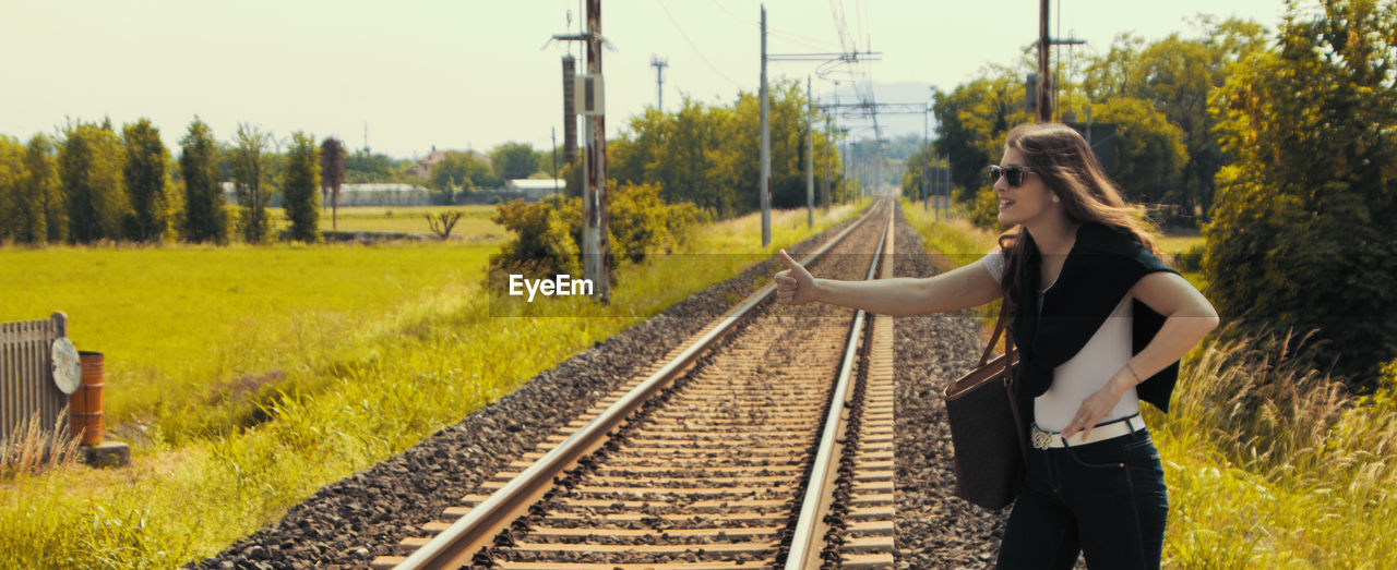 SIDE VIEW OF YOUNG WOMAN STANDING ON RAILROAD TRACKS