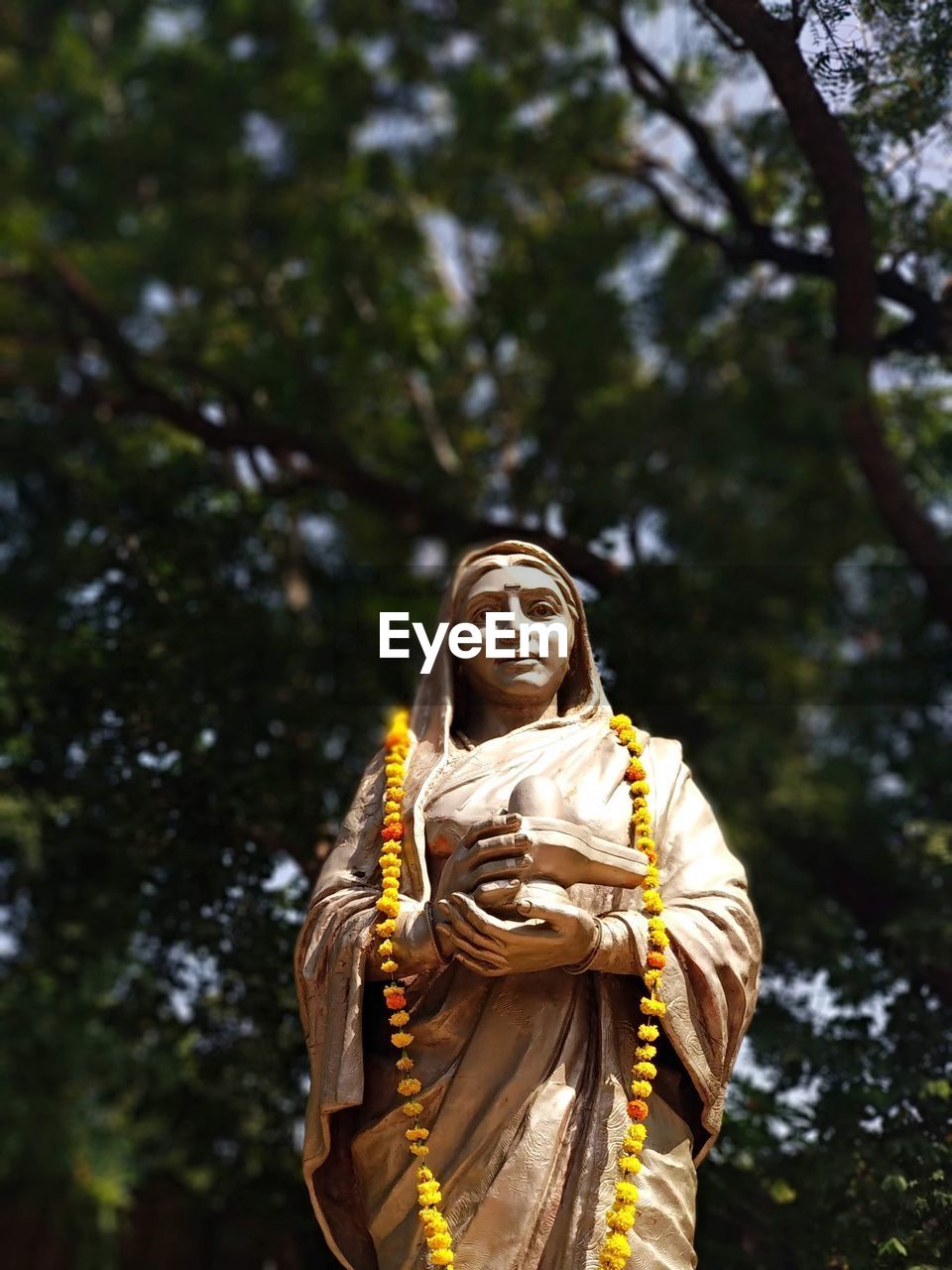 tree, one person, religion, statue, smiling, plant, adult, spirituality, temple, nature, clothing, front view, happiness, belief, outdoors, low angle view, yellow, standing, day, person, traditional clothing, women, emotion, waist up