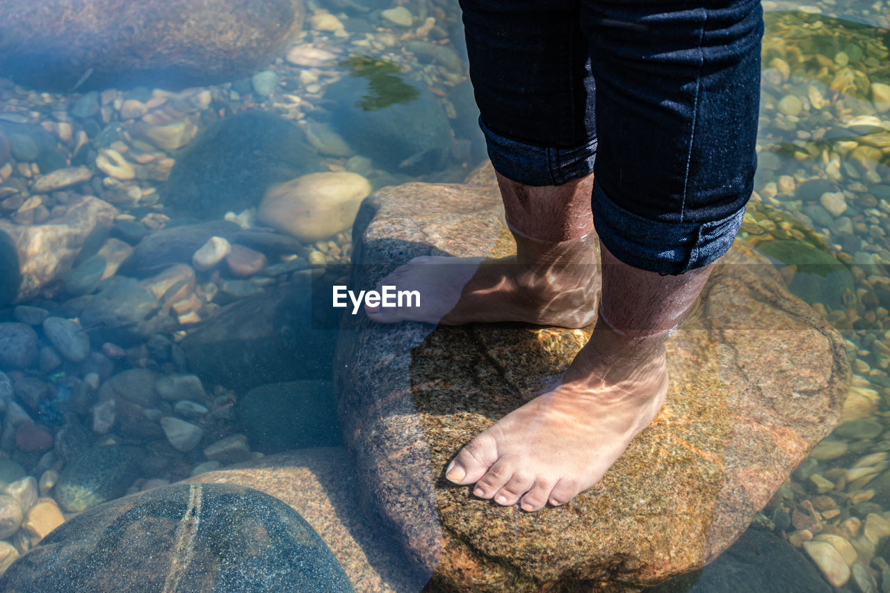 Young girl foot on rock in clear transparent river water from top angle