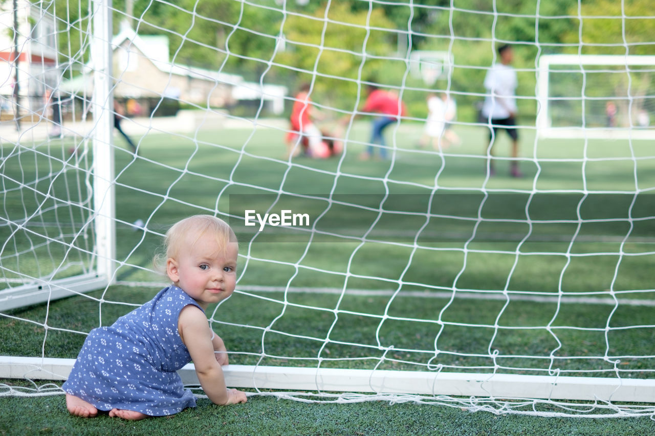 Full length of cute toddler sitting by net on playing field