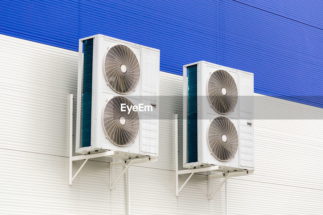 Two double condensing units of air conditioner on blue and white metal industrial wall.