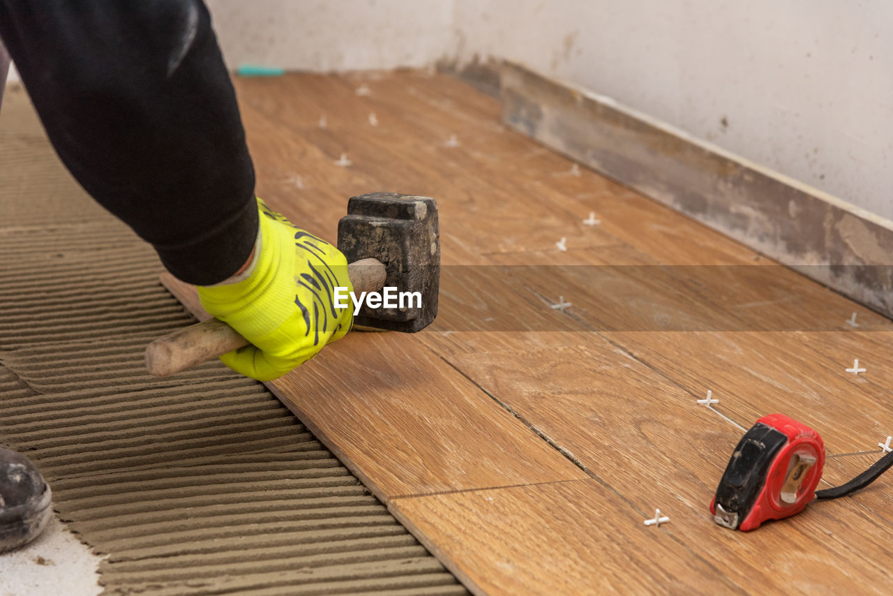 Worker placing ceramic floor tiles on adhesive surface, leveling