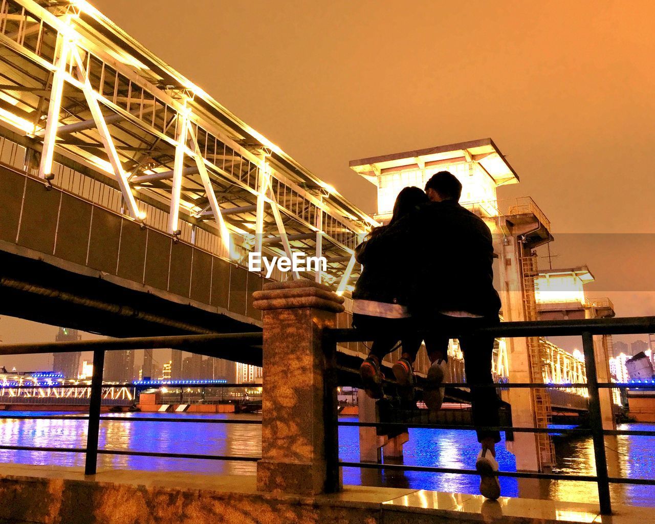 Rear view of people sitting on bridge against clear sky at night