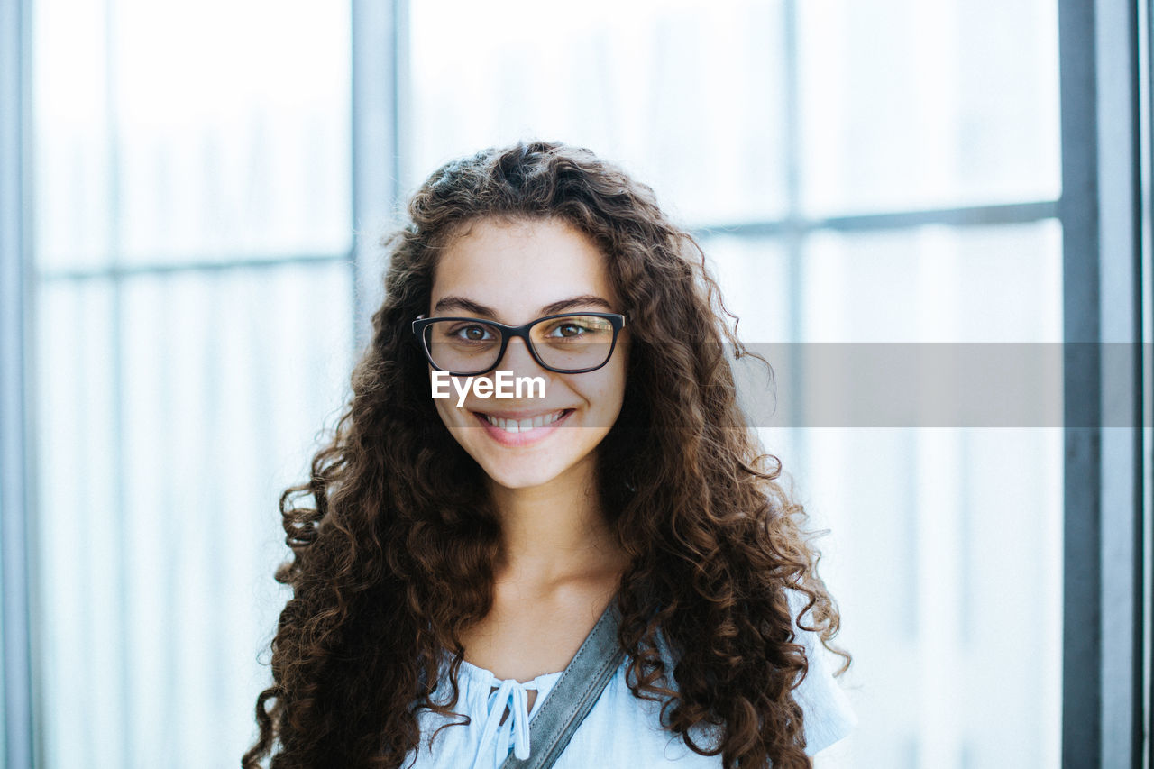 Close-up of beautiful smiling woman against window