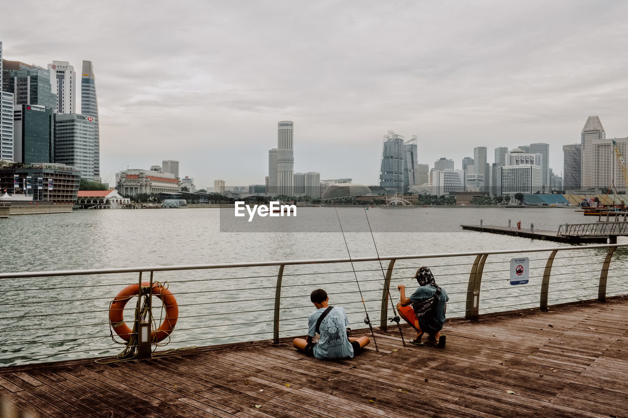 People sitting by river against buildings in city