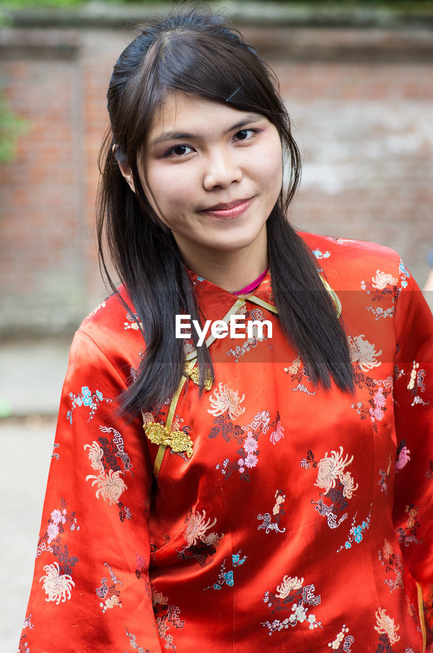 Portrait of woman in red traditional clothing standing against wall