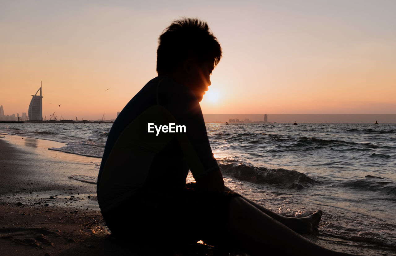 WOMAN STANDING AT BEACH DURING SUNSET