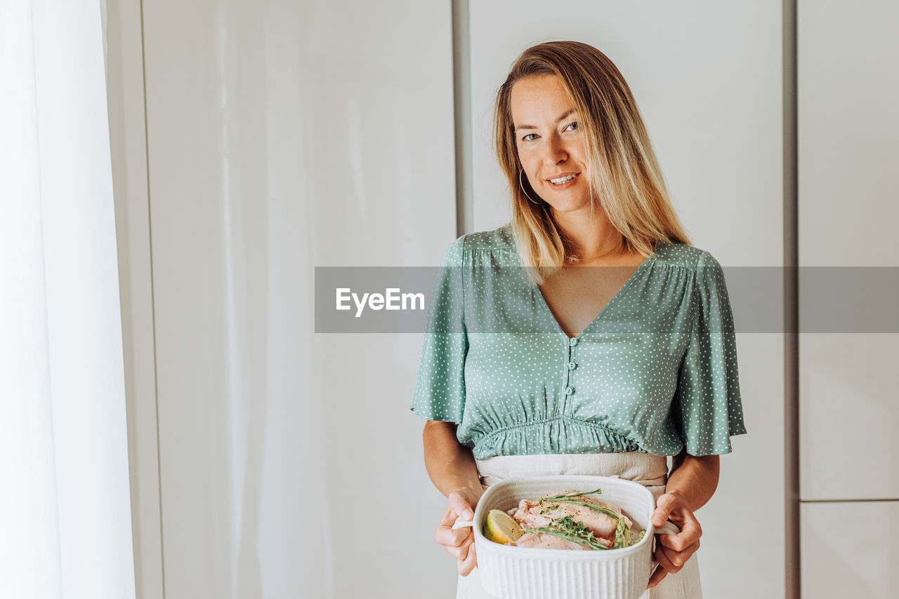 Young blond woman holding a tray with chicken and aromatic herbs