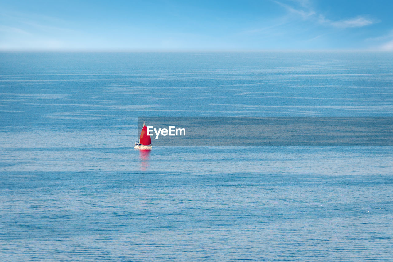 Aerial view of a sailboat with a red sail among the open sea. summer vacation yacht activity. 