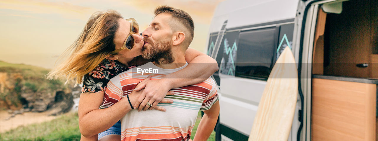 Couple kissing piggybacking next to their camper van during a trip