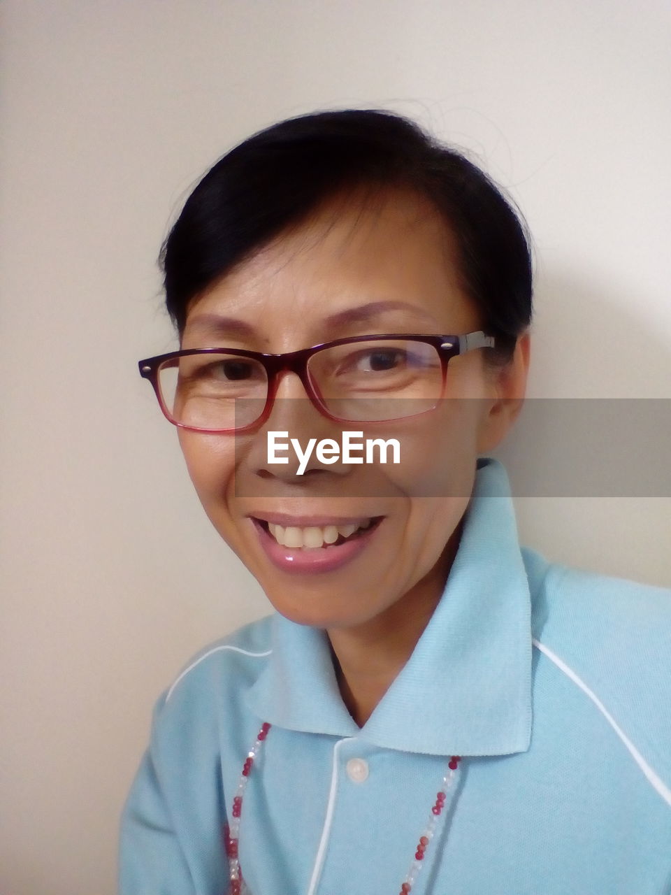 Portrait of smiling woman wearing eyeglasses against wall