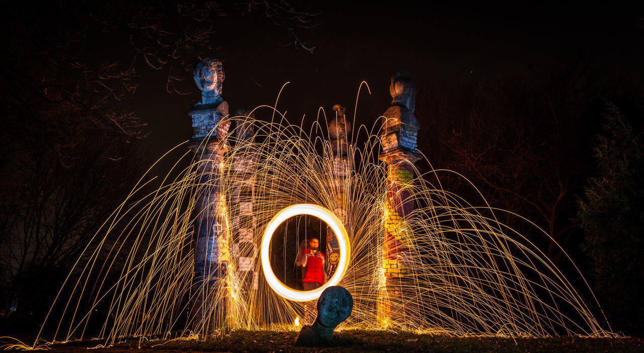 Man standing by illuminated wire wool at night
