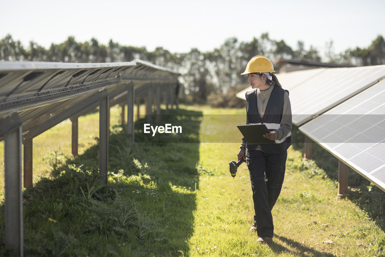 Female maintenance engineer examining solar panels while walking at power station