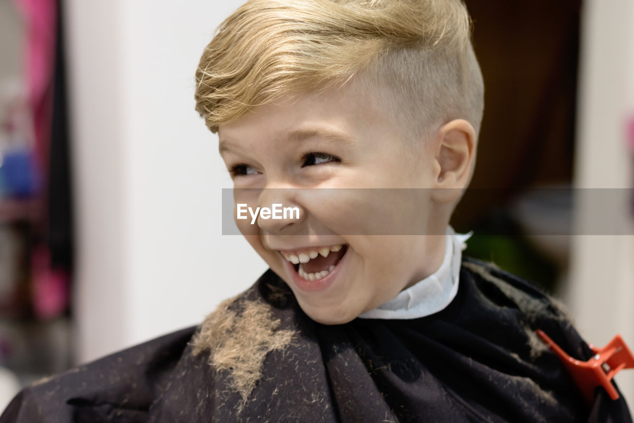 Cute kid laughing while having fun during haircut at hairdresser.