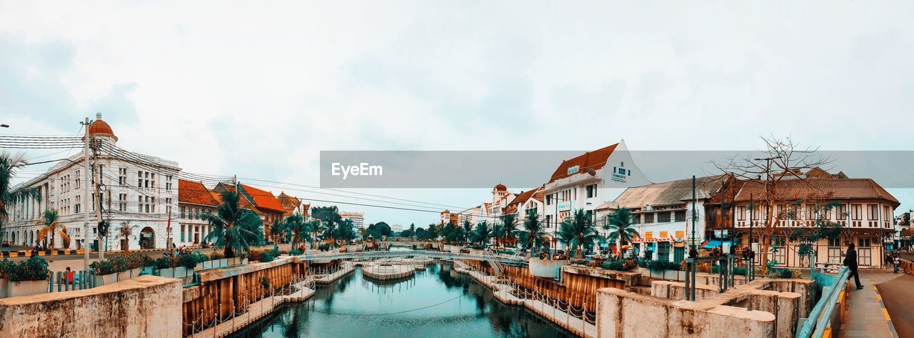 Panoramic view of buildings by canal against sky