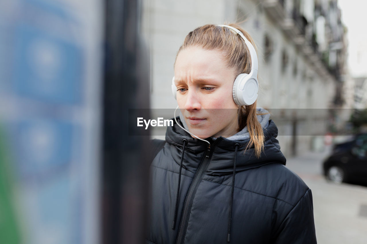 Young woman listening to music using parking meter in city