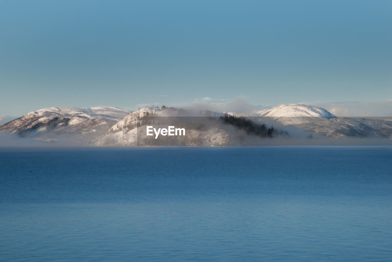 Scenic view of sea and snowcapped mountains against clear blue sky