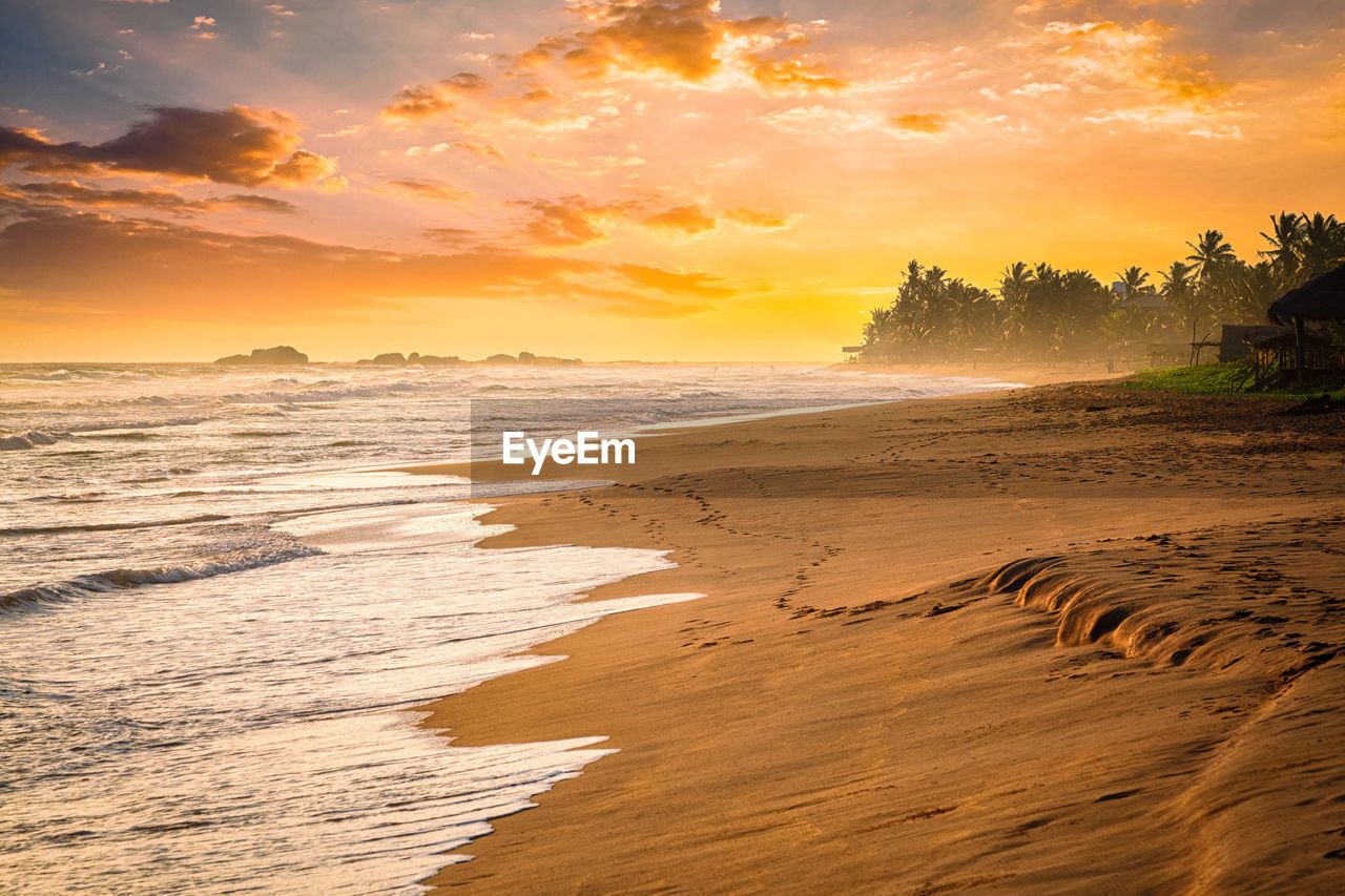 scenic view of beach against cloudy sky during sunset