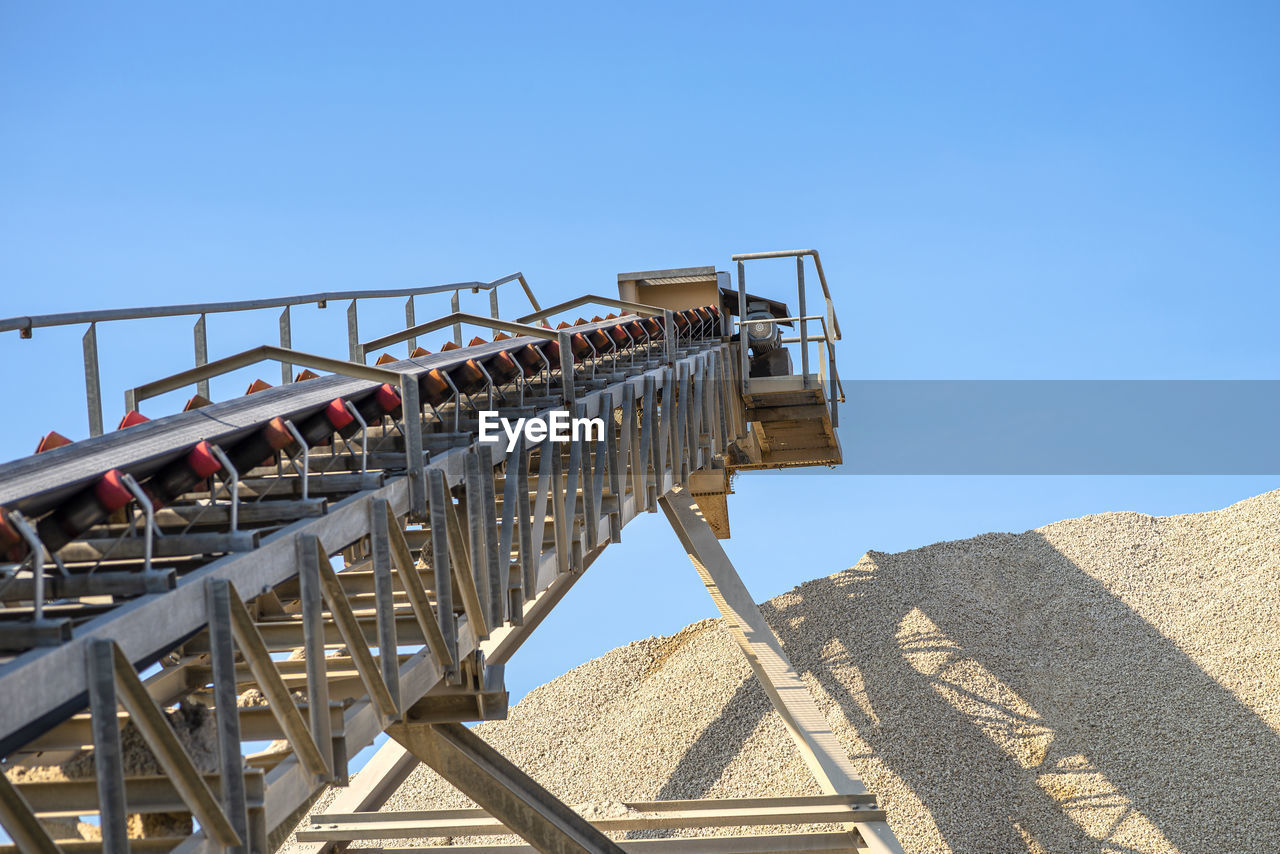 Conveyor belt over heaps of gravel against the blue sky at an industrial cement plant.