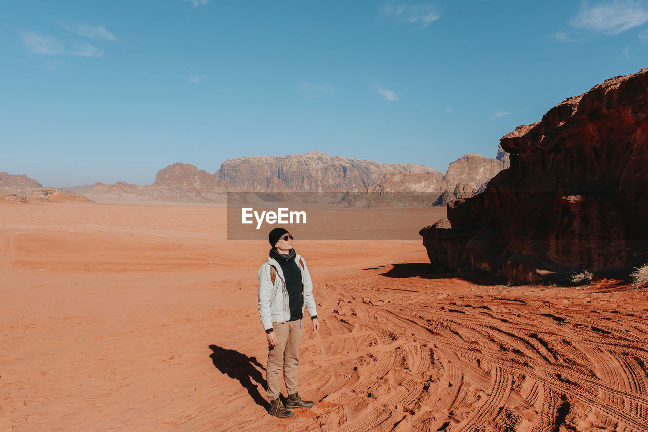 Explorer in outerwear standing on sandy ground of wadi rum sandstone valley on sunny day and admiring amazing scenery during vacation in jordan