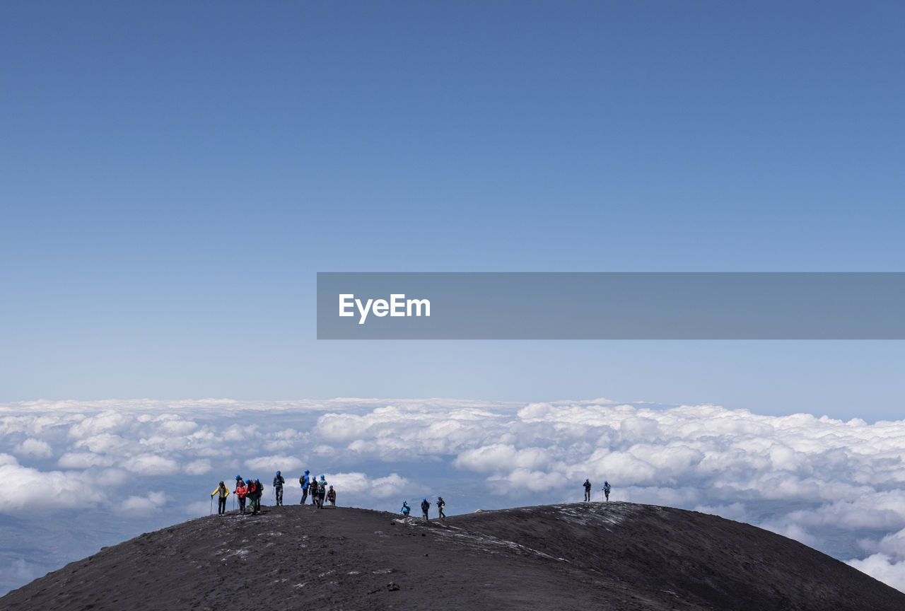 People standing on mountain against cloudy sky