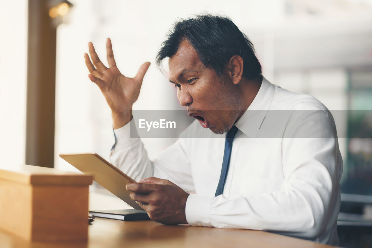 A middle-aged businessman holding a tablet is shocked by what happened to the screen.