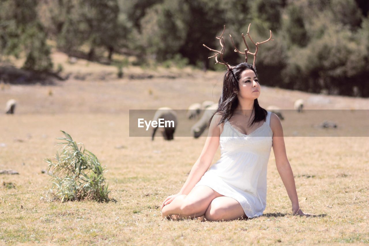 Beautiful woman wearing artificial horn while sitting on field