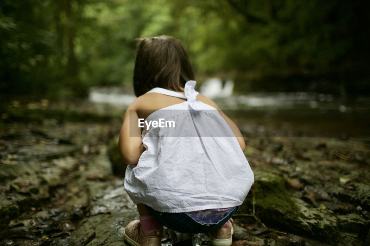 Rear view of girl crouching in forest