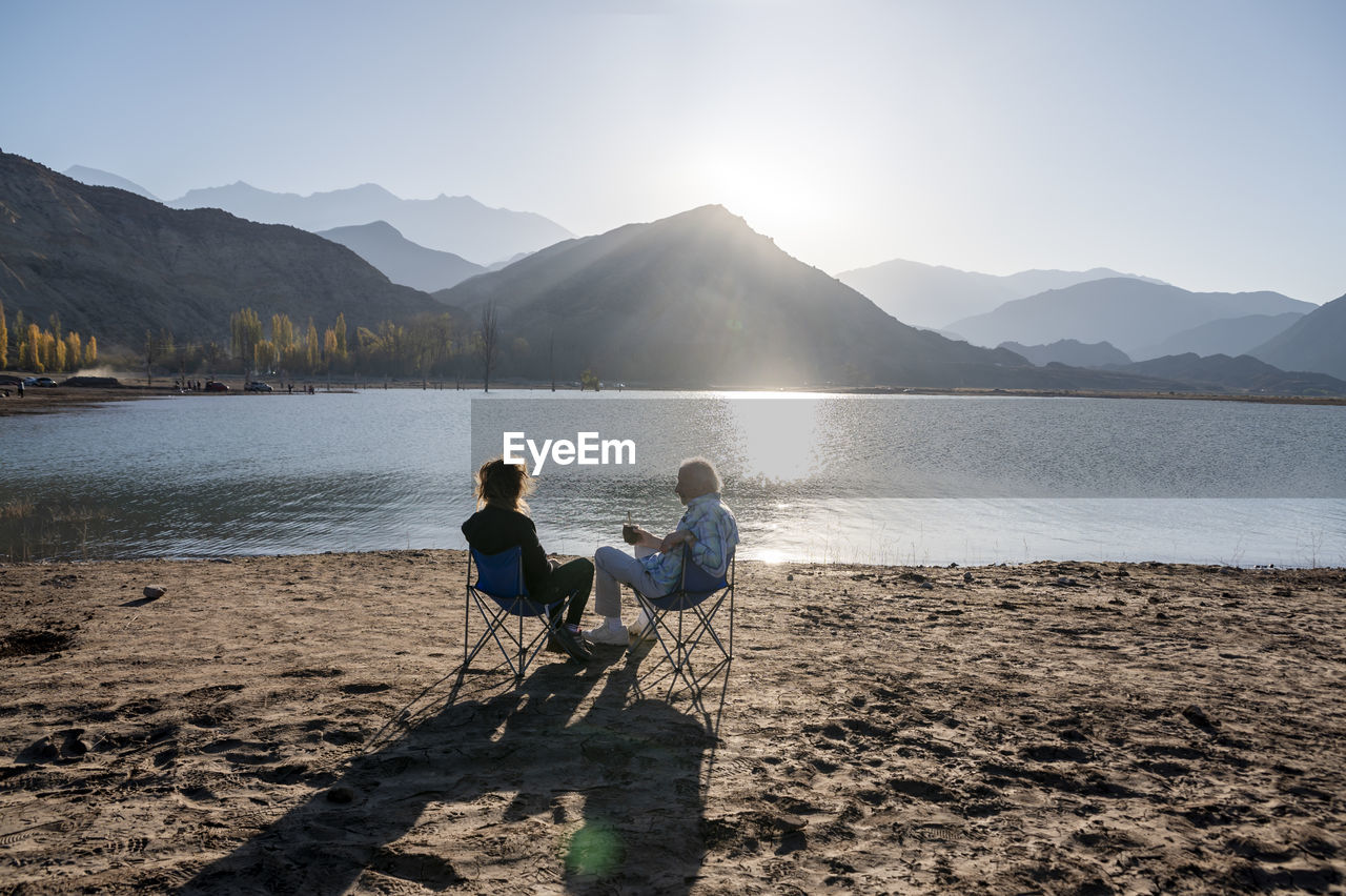 Senior man and his daughter relaxing together sitting outdoors near a lake in nature.