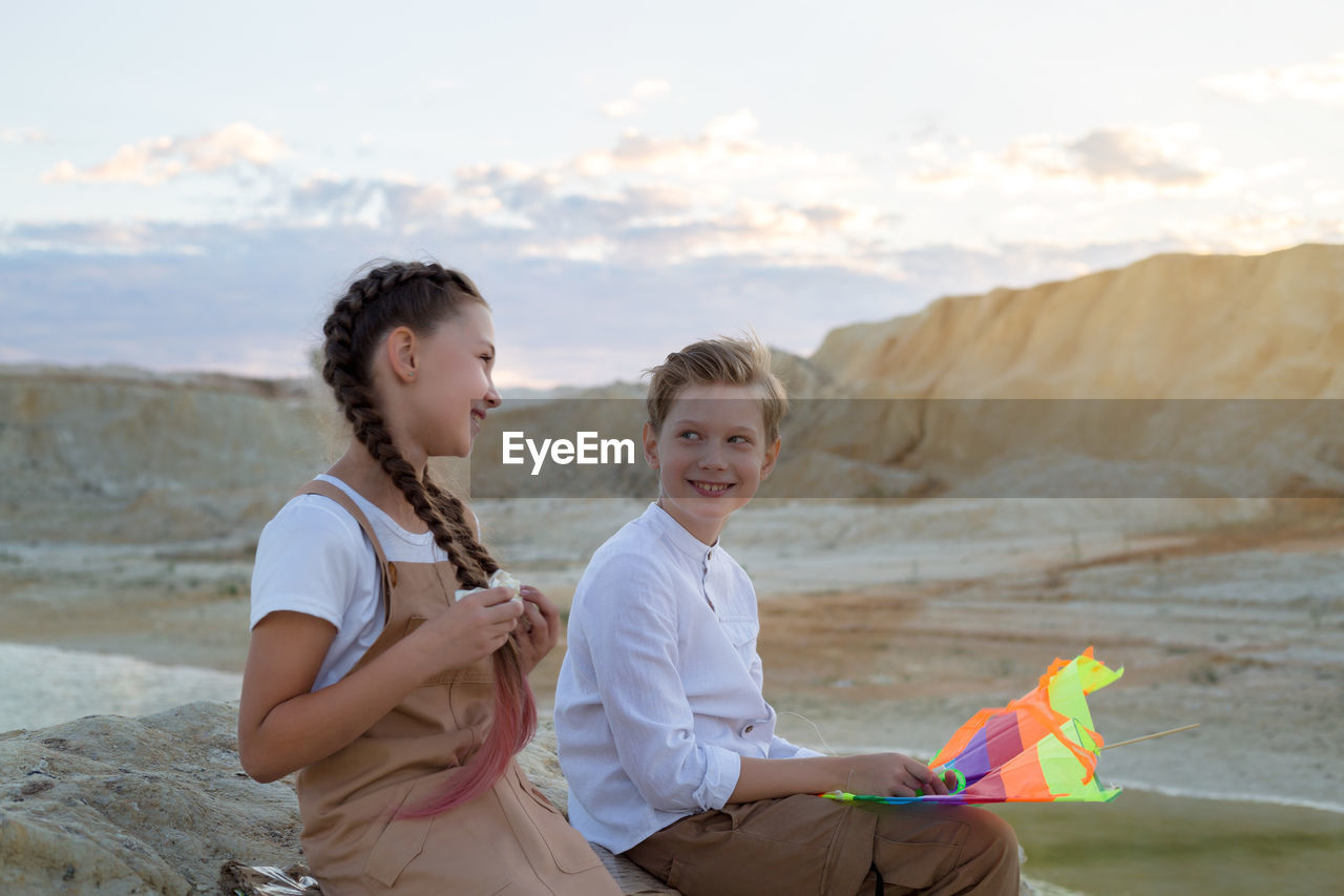 Teenage children talk and laugh while sitting at sunset near the river.