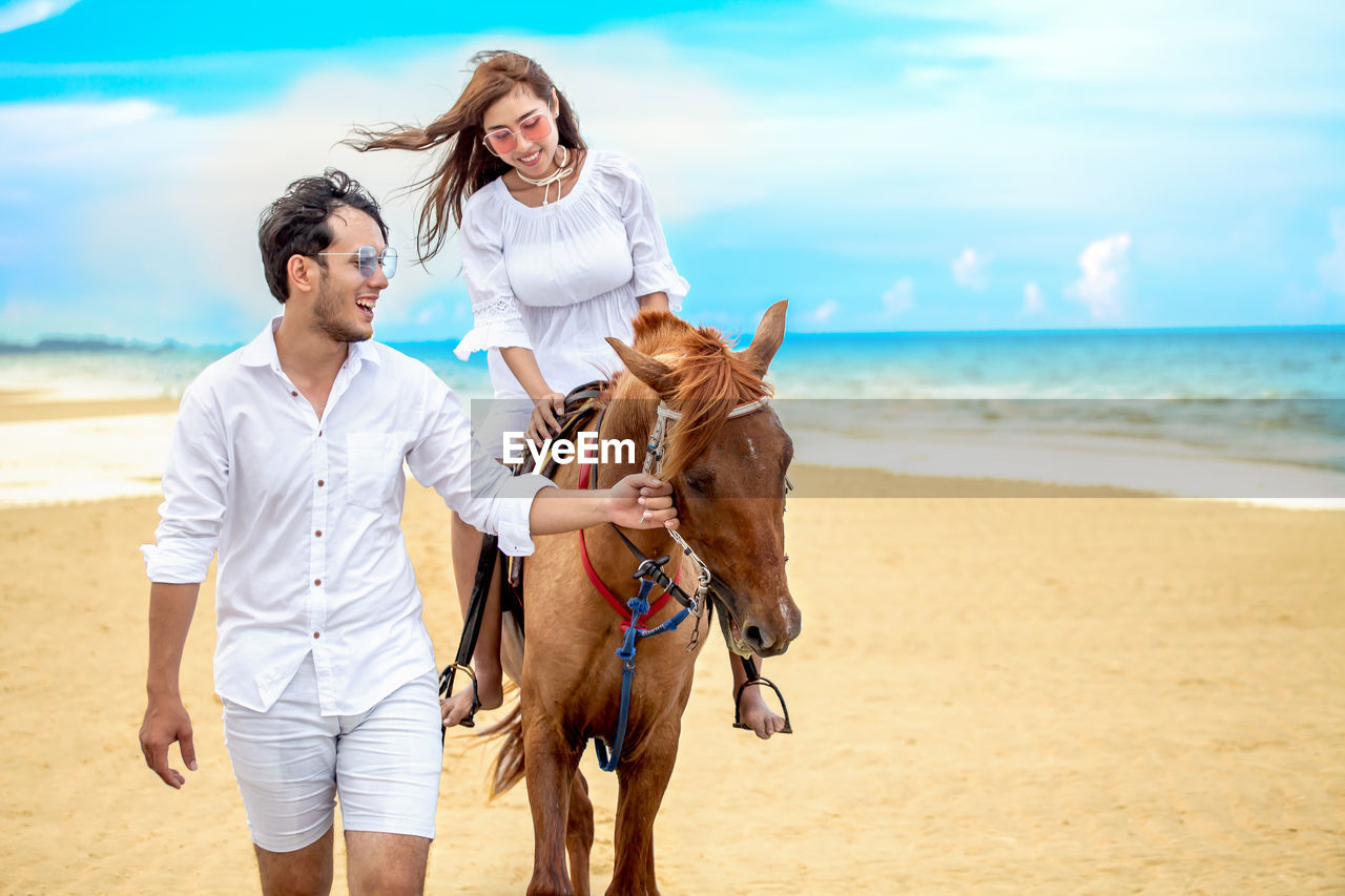 Man with girlfriend riding horse at beach against sky