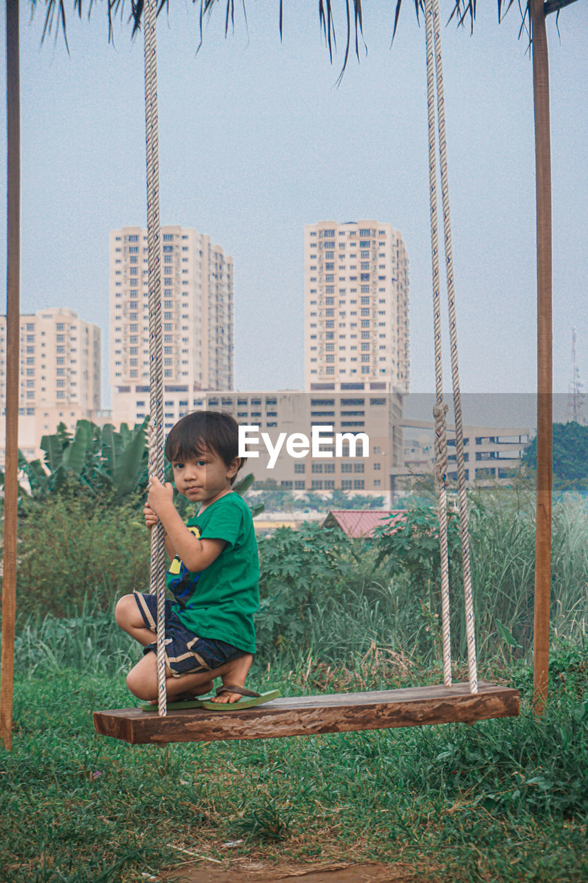 FULL LENGTH OF BOY SITTING ON LAND AGAINST BRIGHT SUN