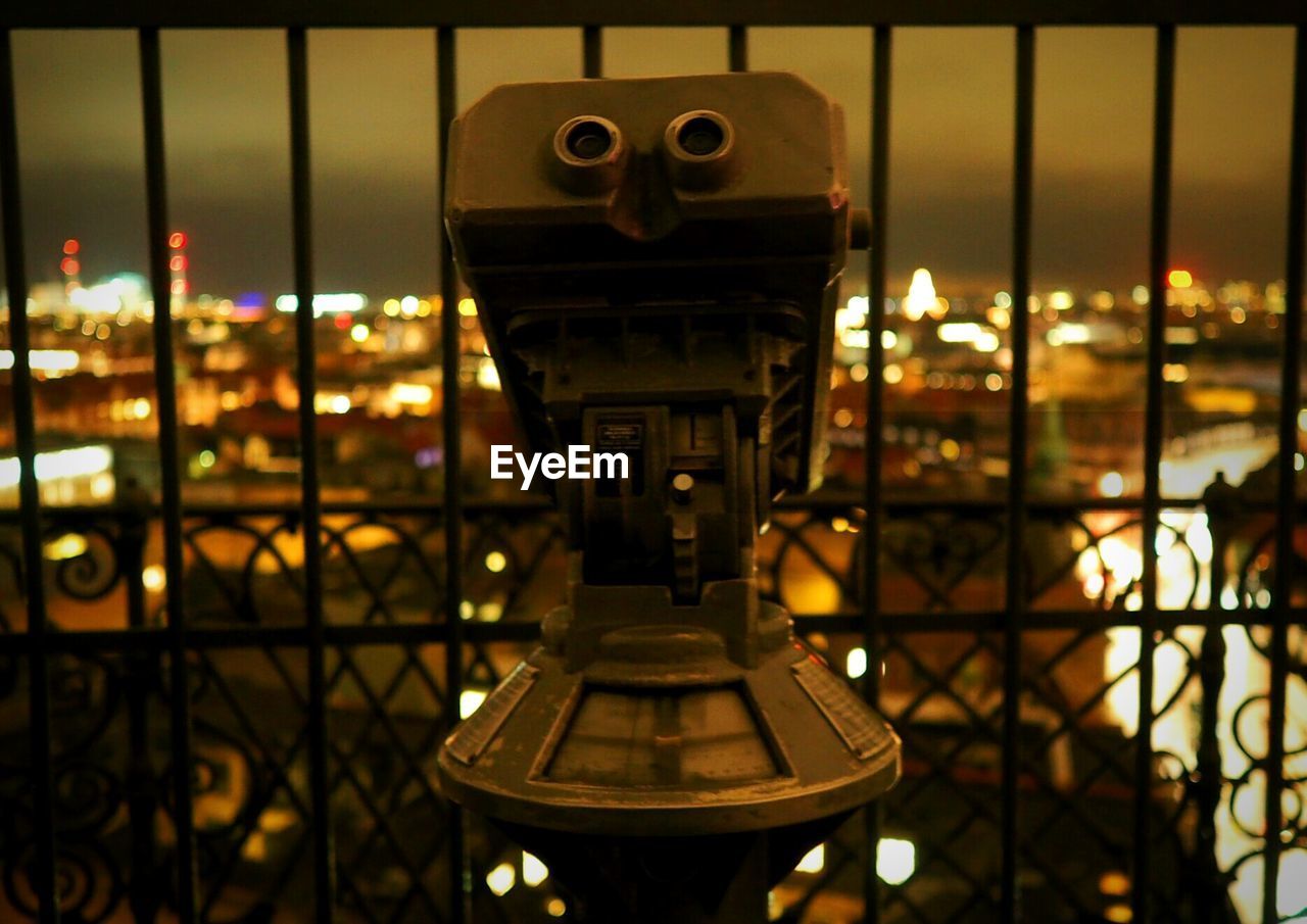 Close-up of coin-operated binoculars against illuminated cityscape
