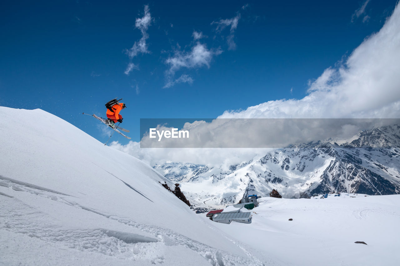 Athlete skier freestyle jumping in orange ski suit in snowy mountains on a sunny day